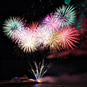 Colorful fireworks exploding over a waterfront celebration at night