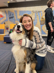 Skyler, a therapy dog, sitting with a smiling student who is hugging him