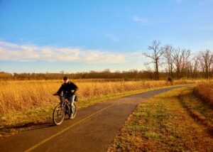 Man riding a bicycle on a paved trail through a grassy field in Five Rivers MetroParks, Ohio, on a sunny day